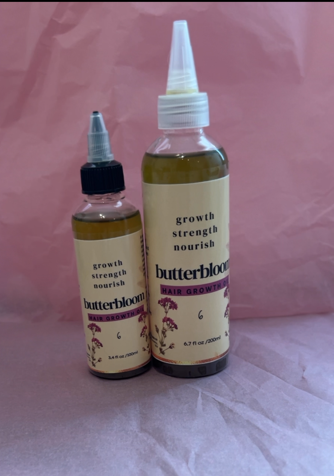 Butterbloom hair growth oil bottle surrounded by various herbs, showcasing its natural ingredients and rich texture.